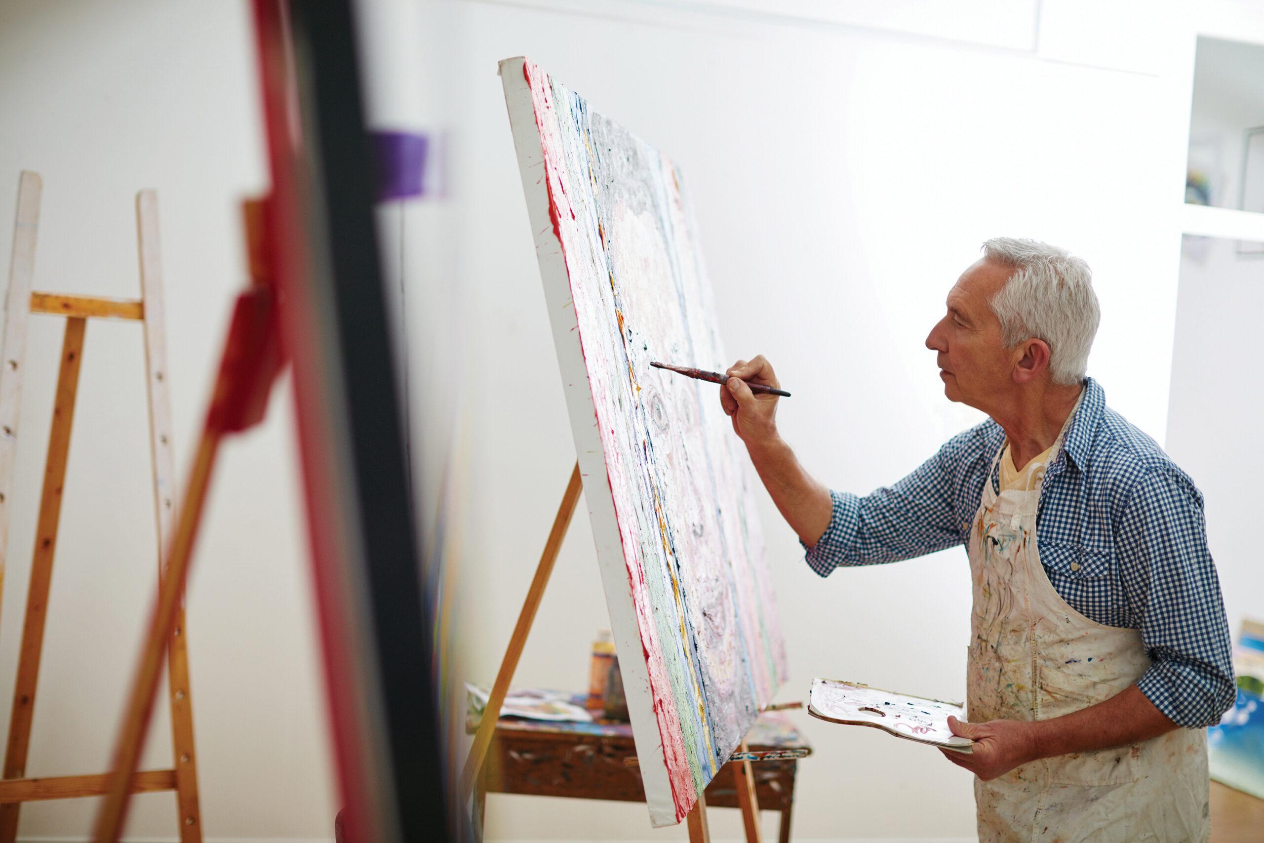 A man concentrates intently on painting on a large canvas.