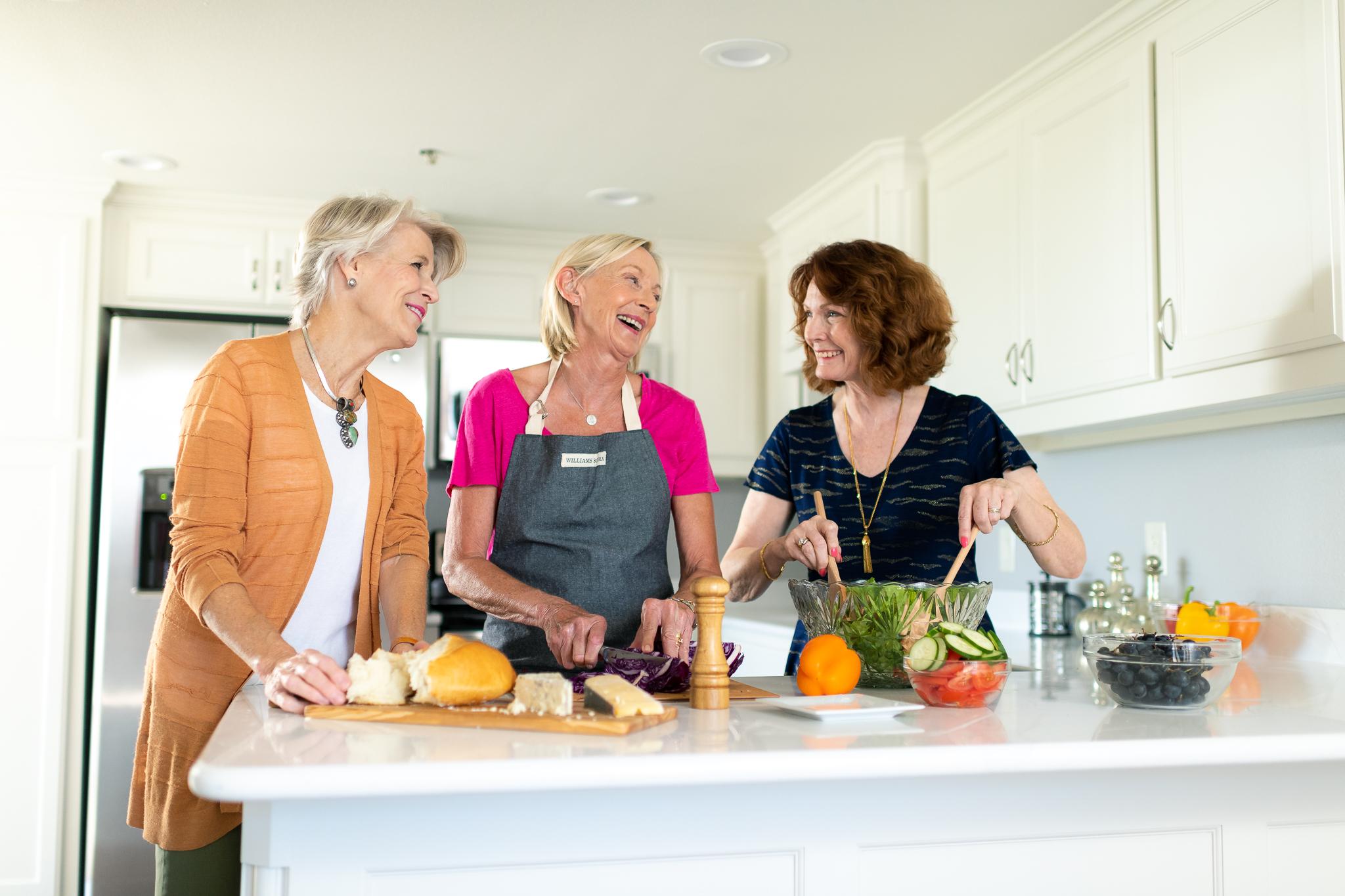 Three happy women smile and cook a healthy meal together.